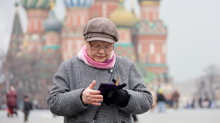 Женщина смотрит на свой мобильный телефон, на заднем плане Красная площадь.