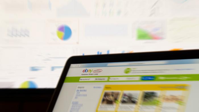 На ноутбуке отображается сайт объявлений eBay со схемами на заднем плане.