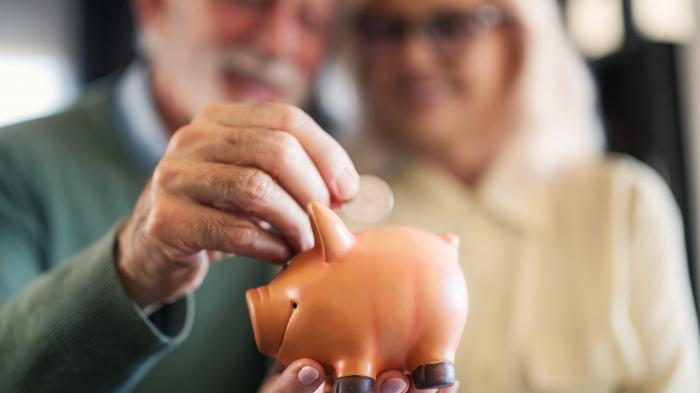 Мужчина кладет монету в копилку, за ней стоит женщина.