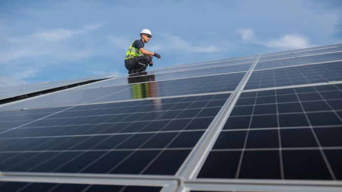 Рабочий на ряде солнечных батарей с инструментом в руке.