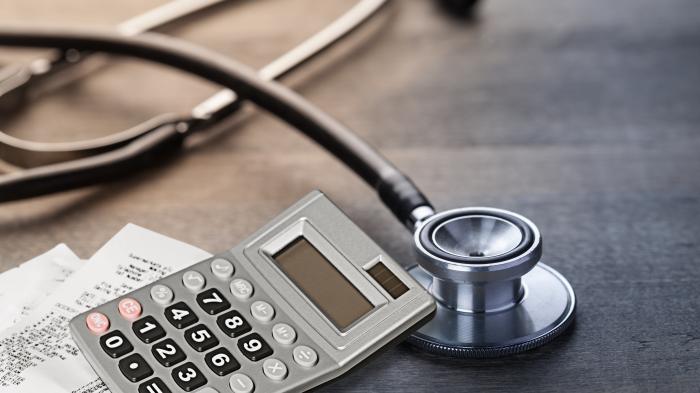 Стетоскоп лежит на деревянном столе рядом с калькулятором и квитанциями.